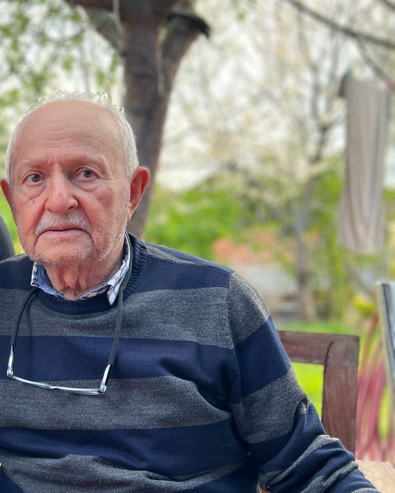 Hikmet Topçu, bahçede ağaçların önünde oturuyor
